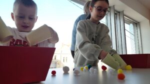 dzieci próbują przenieś pianki za pomocą kubeczków