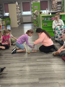 dwie dziewczynki wykonują konkurencję. Z pojemnika wypełnionego woda łowią nakrętki