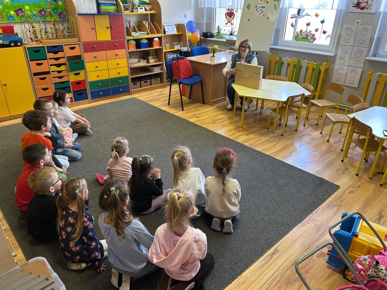 dzieci siedzą na dywanie i słuchają bajki