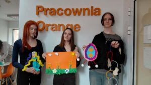 dziewczyny przy napisie pracownia orange prezentują swoje prace