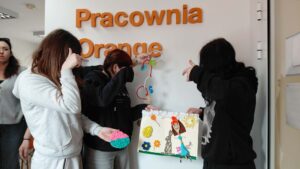 dziewczyny przy napisie pracownia orange prezentują swoje prace