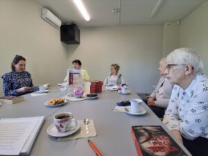 klubowicze siedzą przy stole i dyskutują o książce