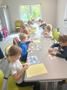 dzieci siedzą przy stołach i układają puzzle