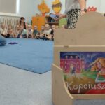 dzieci siedzą na dywanie przed nimi znajduje się teatrzyk kamishibai